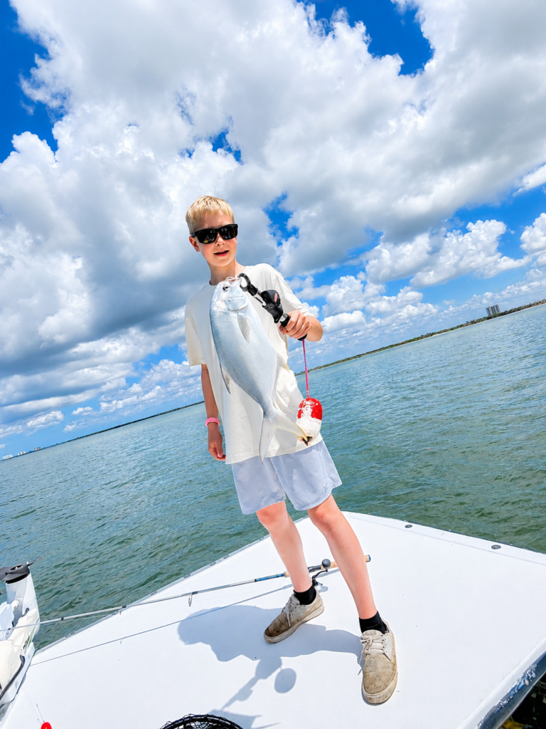 a kid standing on a 27 foot skiff holding a jack that he caught off fort myers beach