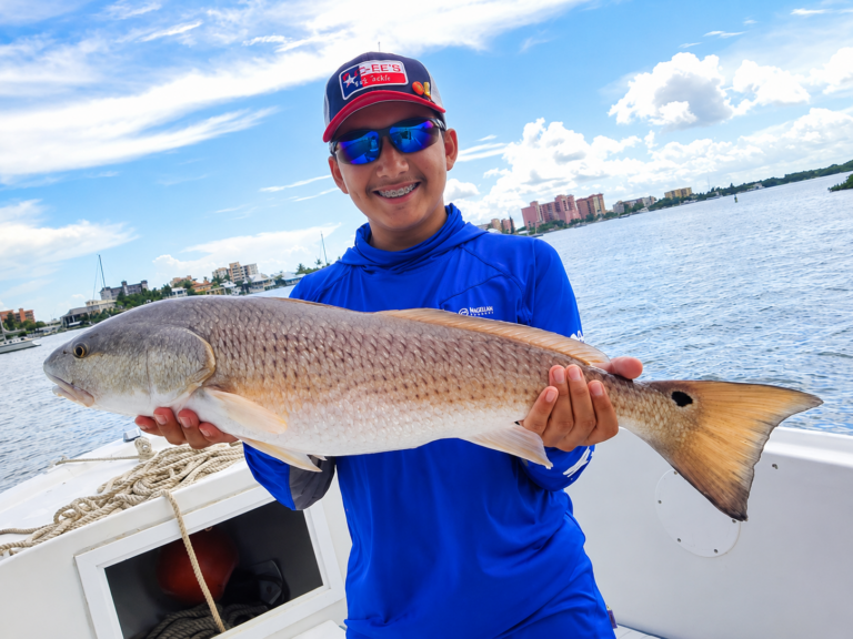 a boy on a 27 ft skiff holding a big redfish