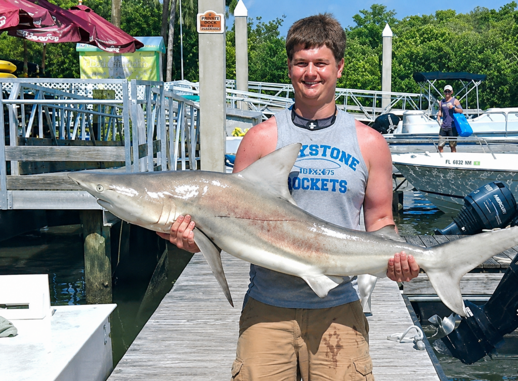 a young man holding a 5 foot lemon shark
