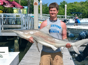 a young man holding a 5 foot lemon shark